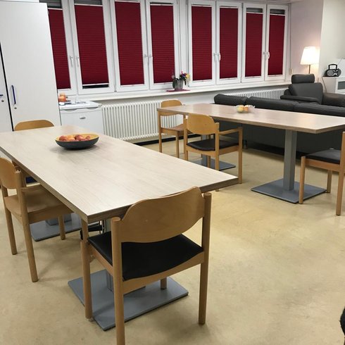 Ein Raum mit zwei leeren Tischen, um die herum Stühle stehen