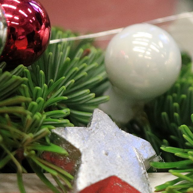 Das Bild zeigt ein Tannenzweig. Darauf liegen ein silberner Stern und eine rote und eine weiße Weihnachtskugel