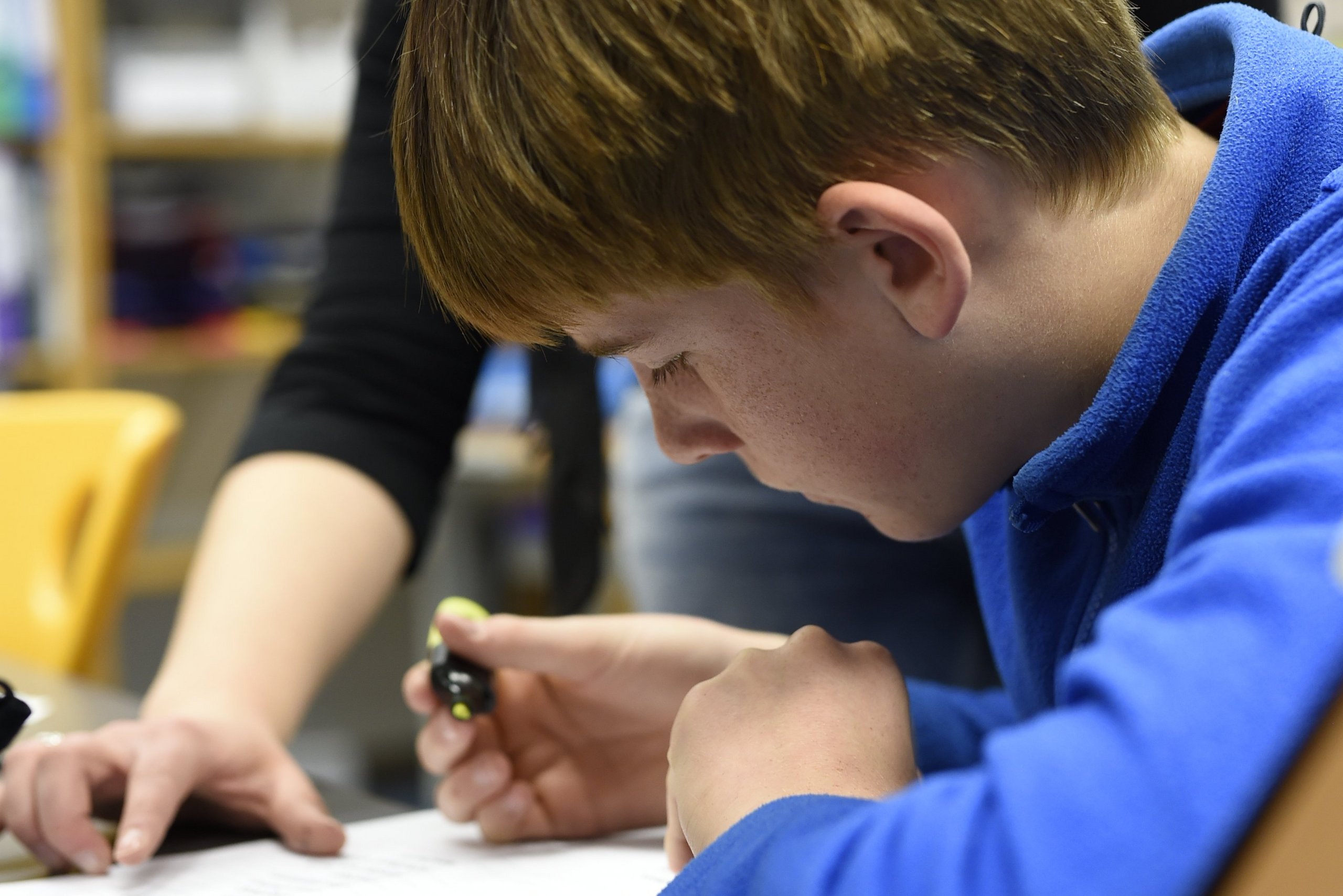 Ein Schüler wird von seiner Lehrerin bei einer Schreibaufgabe unterstützt