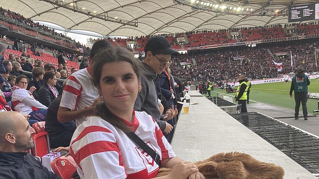 Eine junge Frau im Fußballstadion. Die Frau steht in einem modernen Stadion mit überdachtem Tribünendach an der Brüstung zur Spielfläche. Sie trägt ein Fußballtrikot mit roten und weißen Streifen sowie eine helle Jeans. Vor ihr liegt eine braune Jacke  auf der Brüstung. Eine junge Frau im Fußballstadion. Die Frau steht in einem modernen Stadion mit überdachtem Tribünendach an der Brüstung zur Spielfläche. Sie trägt ein Fußballtrikot mit roten und weißen Streifen sowie eine helle Jeans. Vor ihr liegt eine braune Jacke  auf der Brüstung. 