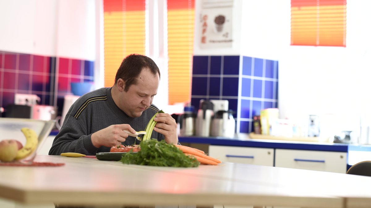 Ein Bewohner sitzt am Küchentisch und schält Gemüse