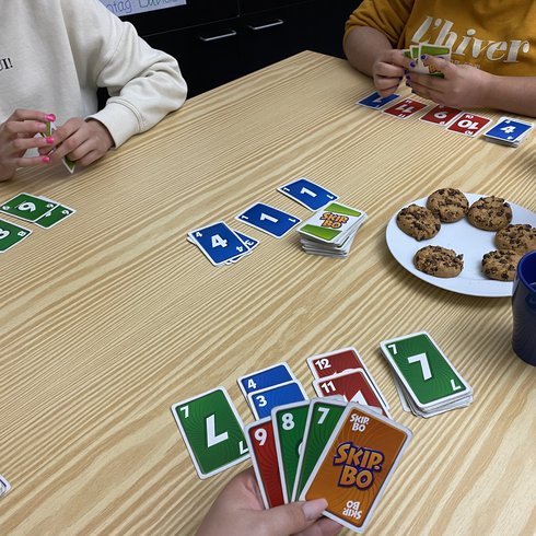 Personen spielen an einem Tisch gemeinsam das Kartenspiel Skip-Bo