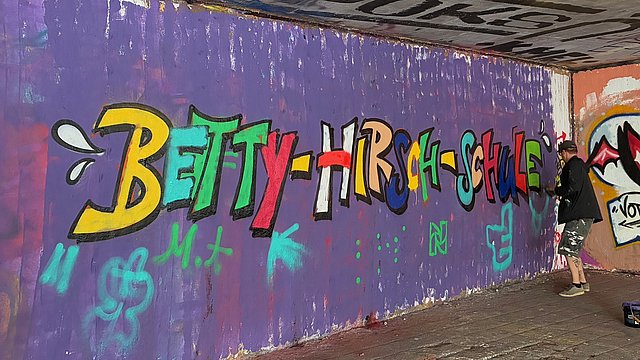 Ein Graffiti auf einer lila Wand zeigt den Schriftzug Betty-Hirsch-Schulzentrum