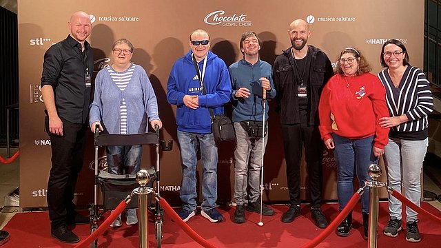 Eine Gruppe erwachsener Personen stehen auf einem roten Teppich vor einer Werbewand