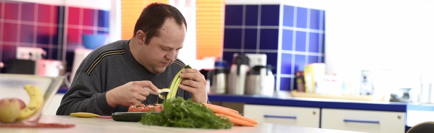 Ein Bewohner sitzt in der Küche und schält Gemüse