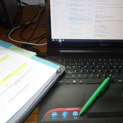 Das Foto zeigt einen Laptop und eine Arbeitsmappe auf einem Schreibtisch