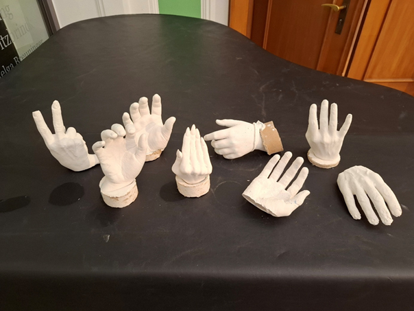 Auf einem dunklen Tisch liegen acht weiße Hände aus Gips in verschiedenen Formen